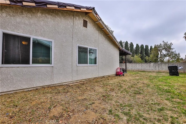 view of side of property featuring a yard, fence, and stucco siding