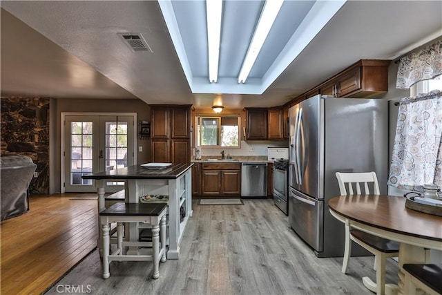 kitchen with appliances with stainless steel finishes, a tray ceiling, light wood-type flooring, and french doors