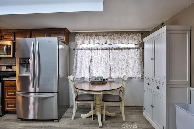 kitchen featuring appliances with stainless steel finishes, brown cabinetry, light countertops, and light wood-style floors