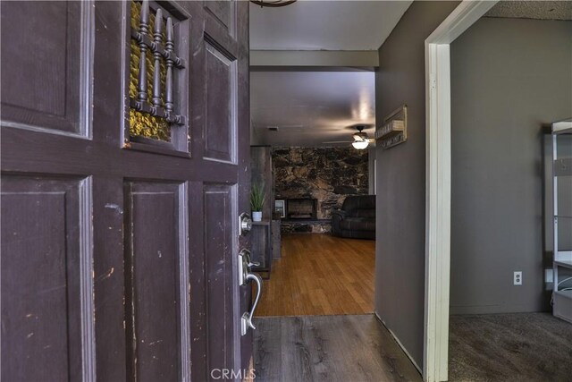 entryway featuring a stone fireplace, dark hardwood / wood-style floors, and ceiling fan