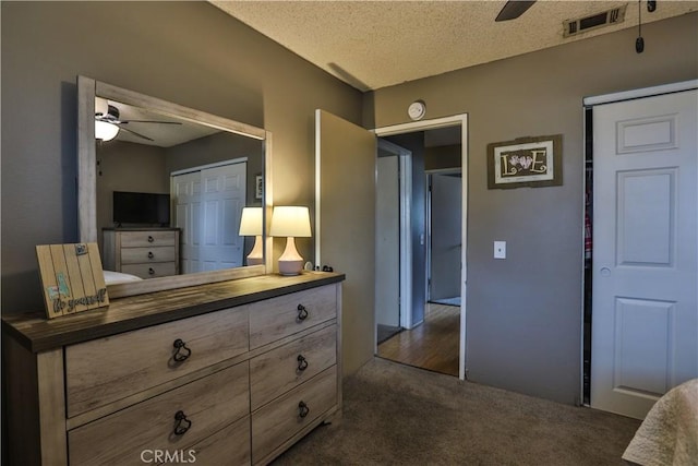 bedroom featuring dark colored carpet, a closet, visible vents, a ceiling fan, and a textured ceiling