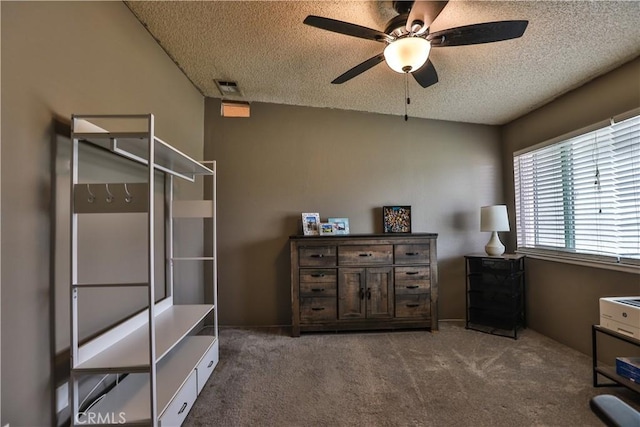 interior space featuring a textured ceiling, dark carpet, visible vents, and a ceiling fan