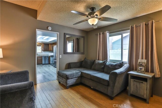 living room featuring ceiling fan, a healthy amount of sunlight, a textured ceiling, and light wood-type flooring