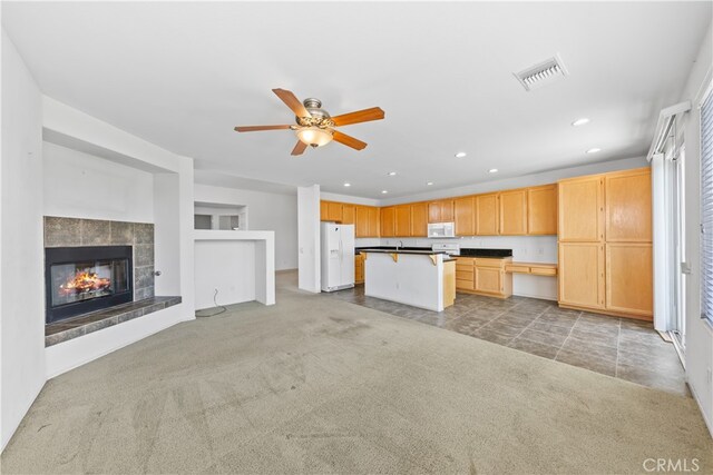 kitchen with a tile fireplace, a kitchen island, light brown cabinetry, carpet floors, and white appliances