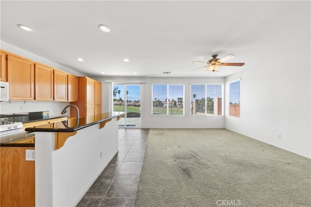 kitchen featuring ceiling fan, dark stone counters, a kitchen breakfast bar, and dark carpet