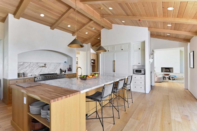 kitchen with pendant lighting, white cabinetry, a breakfast bar area, a large island with sink, and stainless steel range