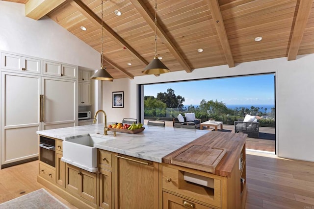 kitchen with white cabinetry, sink, light stone counters, light hardwood / wood-style floors, and a center island with sink