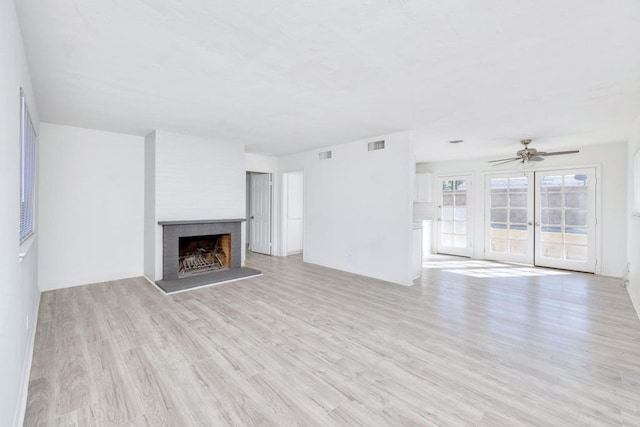 unfurnished living room with a brick fireplace, ceiling fan, and light wood-type flooring