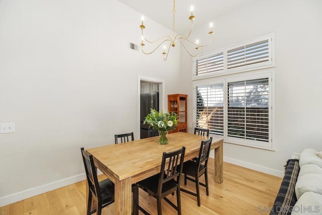 dining area with a notable chandelier, a towering ceiling, and light hardwood / wood-style floors