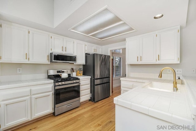 kitchen featuring sink, tile countertops, stainless steel appliances, and white cabinets