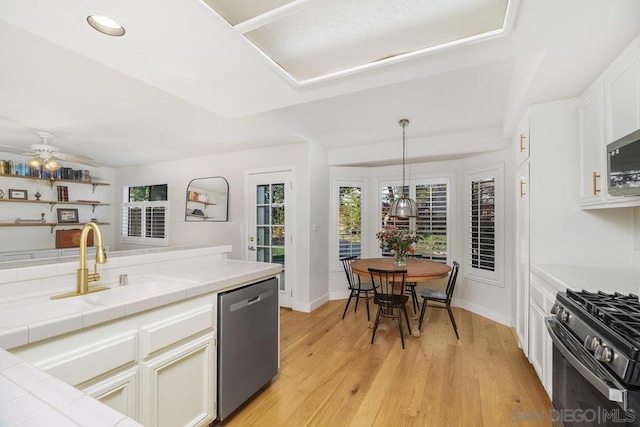 kitchen featuring white cabinetry, hanging light fixtures, tile counters, and stainless steel appliances