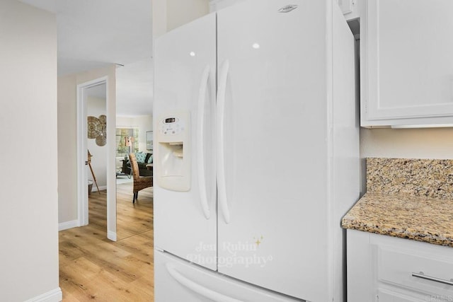 interior space featuring white refrigerator with ice dispenser, light stone countertops, light hardwood / wood-style floors, and white cabinets