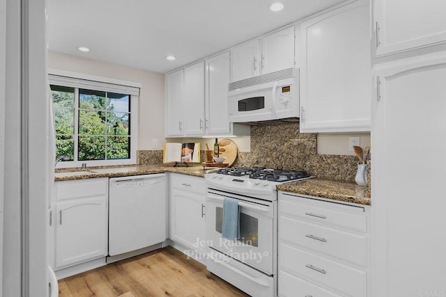 kitchen with tasteful backsplash, white cabinetry, white appliances, and dark stone counters