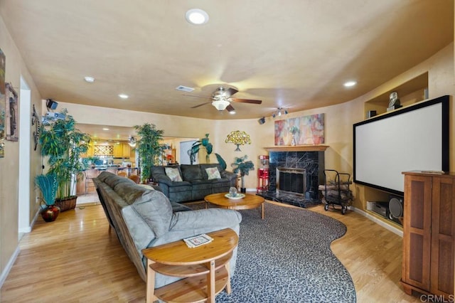 living room with light hardwood / wood-style floors, a premium fireplace, and ceiling fan