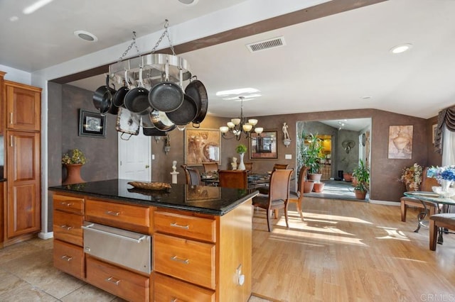 kitchen with dark stone countertops, a center island, a notable chandelier, light hardwood / wood-style floors, and vaulted ceiling