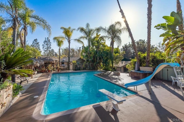 view of swimming pool with a patio area, a hot tub, a diving board, and a water slide