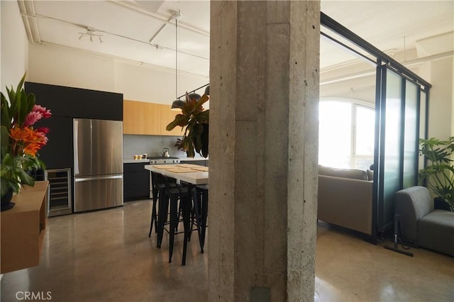 kitchen with light brown cabinetry, a kitchen breakfast bar, stainless steel refrigerator, and beverage cooler