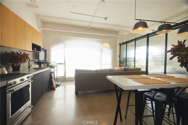 kitchen with hanging light fixtures, stainless steel range with gas cooktop, sink, and a kitchen bar