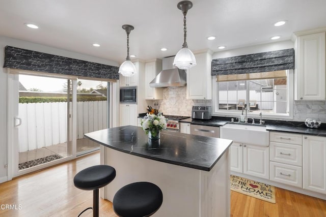 kitchen featuring a kitchen island, pendant lighting, sink, white cabinets, and wall chimney exhaust hood