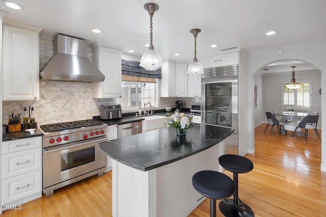 kitchen featuring white cabinetry, hanging light fixtures, high end appliances, a center island, and wall chimney range hood