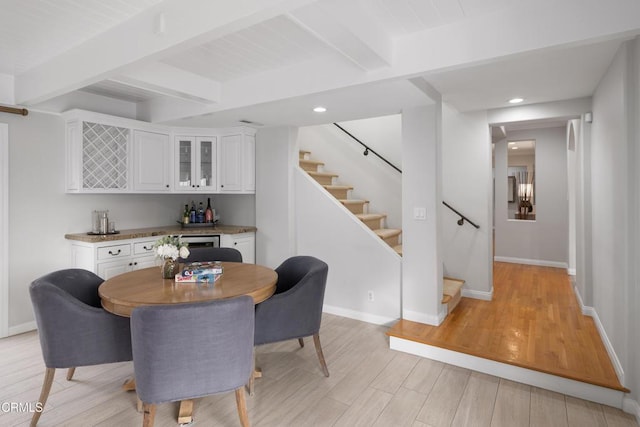 dining space with beam ceiling, light hardwood / wood-style flooring, and bar area