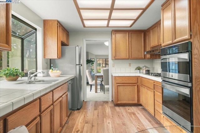 kitchen with appliances with stainless steel finishes, tile counters, light hardwood / wood-style floors, and sink