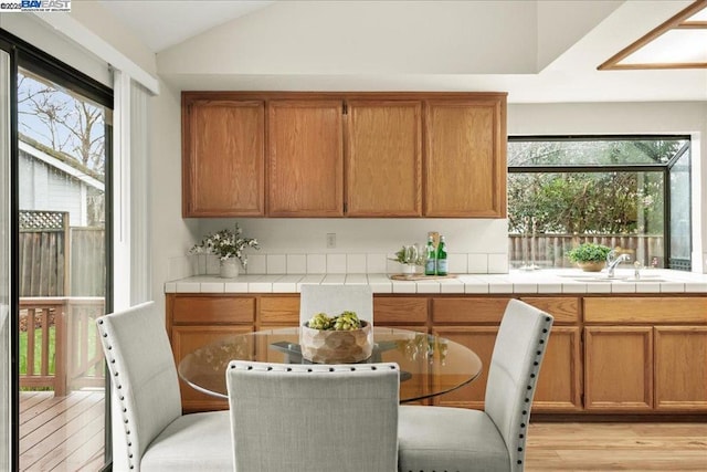 kitchen with light wood-type flooring, sink, tile counters, and vaulted ceiling