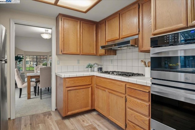 kitchen featuring appliances with stainless steel finishes, tile countertops, light hardwood / wood-style floors, and backsplash