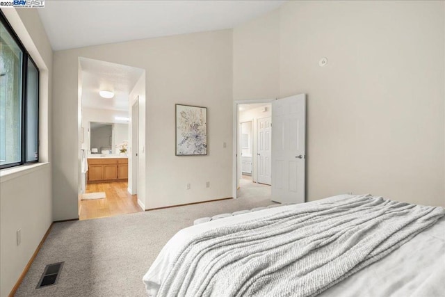 bedroom featuring lofted ceiling, light carpet, and ensuite bath