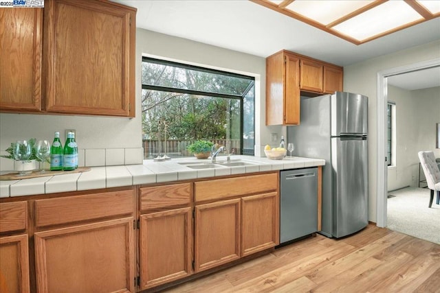 kitchen with stainless steel appliances, sink, tile counters, and light hardwood / wood-style flooring