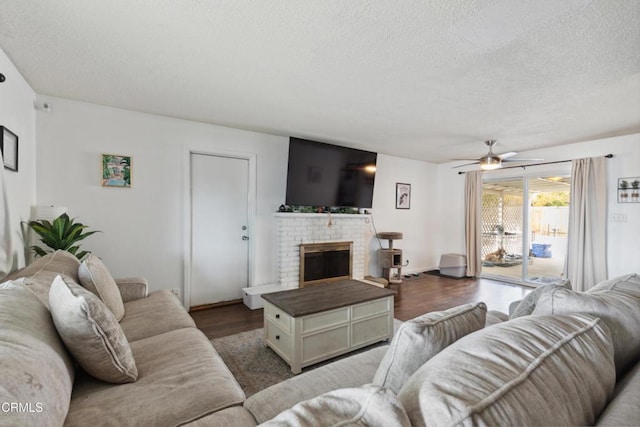 living room with a brick fireplace, dark wood-type flooring, a textured ceiling, and ceiling fan