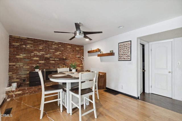 dining area with hardwood / wood-style flooring, ceiling fan, and brick wall