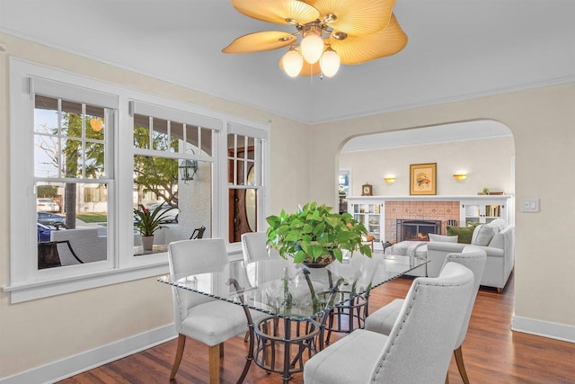 dining area with hardwood / wood-style flooring, ceiling fan, ornamental molding, and a fireplace