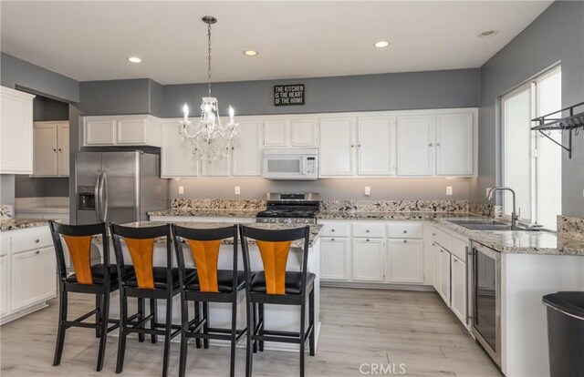 kitchen with appliances with stainless steel finishes, wine cooler, white cabinets, and decorative light fixtures