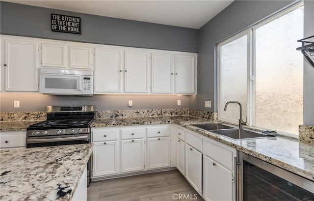 kitchen with beverage cooler, white microwave, a sink, and white cabinets