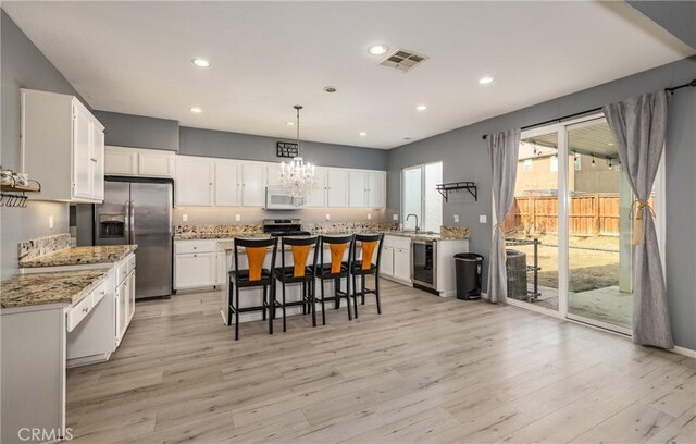 kitchen featuring hanging light fixtures, stainless steel appliances, white cabinets, a kitchen island, and beverage cooler