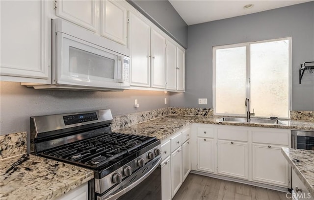 kitchen featuring gas range, light wood-style flooring, white microwave, white cabinetry, and a sink