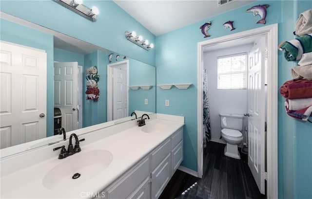 bathroom with toilet, double vanity, a sink, and wood finished floors