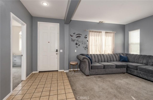 living area featuring light tile patterned floors, baseboards, visible vents, light colored carpet, and beamed ceiling