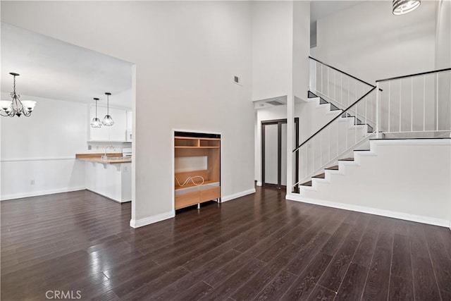 unfurnished living room with sink, a towering ceiling, dark hardwood / wood-style floors, and a chandelier