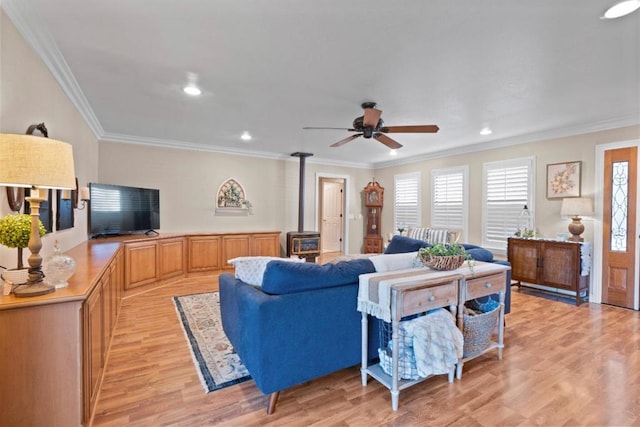 living room featuring crown molding, ceiling fan, light wood-type flooring, and a wood stove