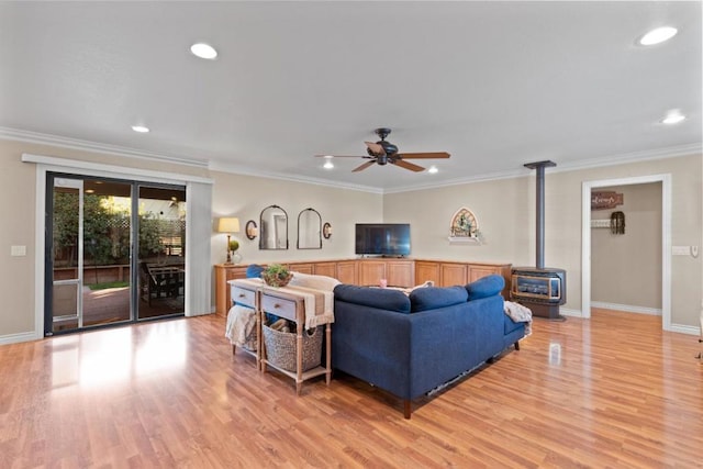 living room featuring crown molding, ceiling fan, light hardwood / wood-style floors, and a wood stove