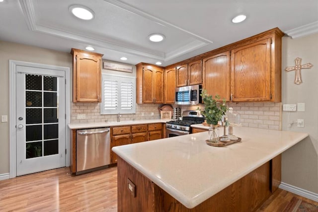 kitchen with appliances with stainless steel finishes, tasteful backsplash, light hardwood / wood-style floors, kitchen peninsula, and a raised ceiling