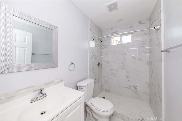 bathroom featuring a tile shower, vanity, and toilet