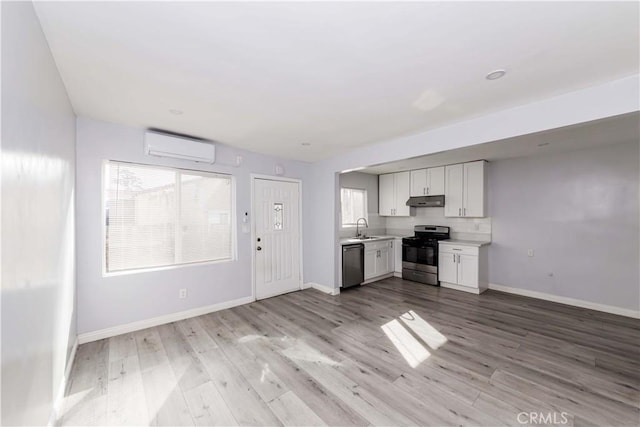 kitchen with sink, appliances with stainless steel finishes, white cabinetry, an AC wall unit, and light wood-type flooring