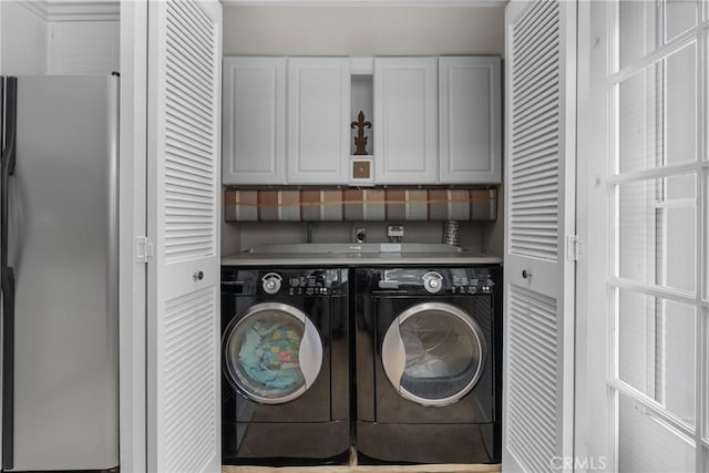 clothes washing area featuring separate washer and dryer and cabinets