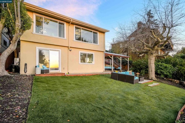 back house at dusk with an outdoor living space and a lawn