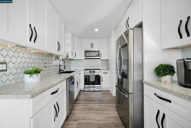 kitchen with sink, backsplash, stainless steel appliances, light stone counters, and white cabinets