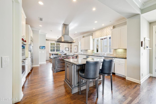 kitchen featuring a kitchen bar, crown molding, island range hood, a kitchen island, and white cabinets