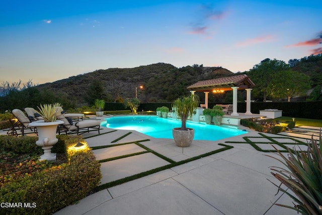 pool at dusk with a mountain view, a gazebo, and a patio area